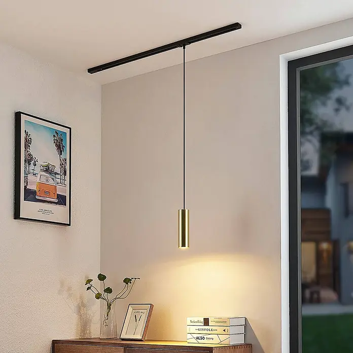 Lindby LED-Spannseilsystem Linaro - schwarz, messing / gold - Eine goldfarbene Pendelleuchte hängt von einer schwarzen Schiene an der Decke und beleuchtet einen darunter liegenden Schrank.
