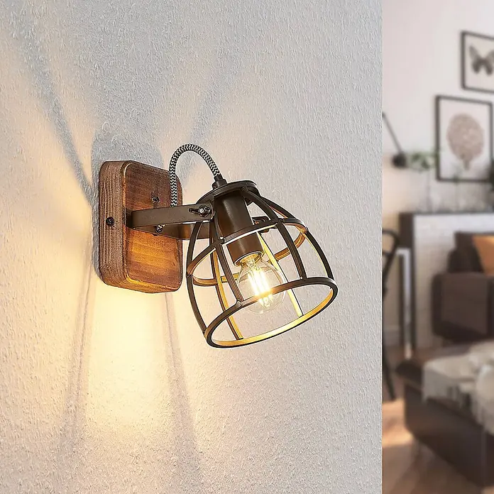 Lindby Wandleuchte innen in schwarz, braun, Wandstrahler -  - Industrielle Wandleuchte mit dunklem Holzsockel und dunklem Metallkäfigschirm, beleuchtet eine strukturierte Wand in einem Zuhause.