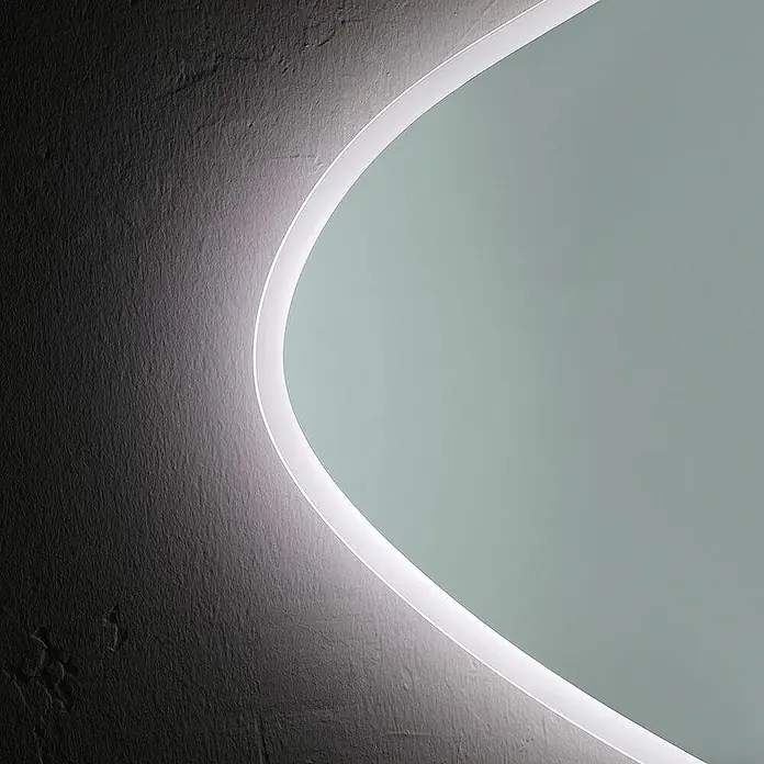 Kiamami Valentina Lichtspiegel - 29 x 750 cm, Farblos - Gekrümmtes, hinterleuchtetes Lichtpaneel wirft ein sanftes weißes Leuchten auf eine strukturierte dunkle Wand. Sorgt für stimmungsvolle Beleuchtung.