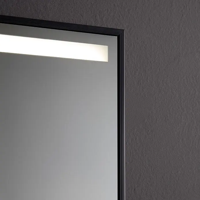 Kiamami Valentina Lichtspiegel - 20 x 700 cm, Chrom - Nahaufnahme eines gerahmten Spiegels mit integriertem horizontalen LED-Lichtstreifen oben, an einer dunklen strukturierten Wand.