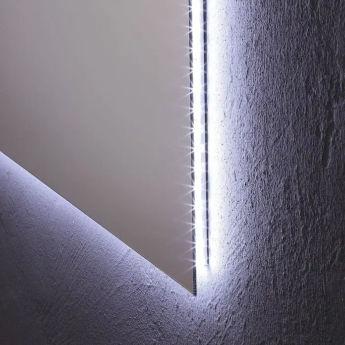 Kiamami Valentina Lichtspiegel - 22 x 600 cm, Farblos - Spiegel mit integrierter LED-Beleuchtung, die Licht auf eine texturierte Wand wirft.