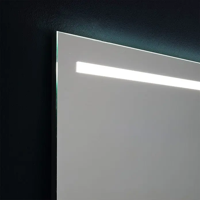 Kiamami Valentina Lichtspiegel - 25 x 700 cm, Farblos - Nahaufnahme eines rahmenlosen Spiegels mit integriertem, horizontalen LED-Lichtstreifen, der Oberfläche und Wand beleuchtet.