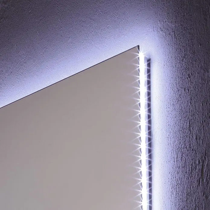 Kiamami Valentina Lichtspiegel - 22 x 700 cm, Farblos - Ecke eines hinterleuchteten Flachpaneels mit sichtbarem LED-Streifen, der eine strukturierte Wand mit kühlem weißem Licht beleuchtet.