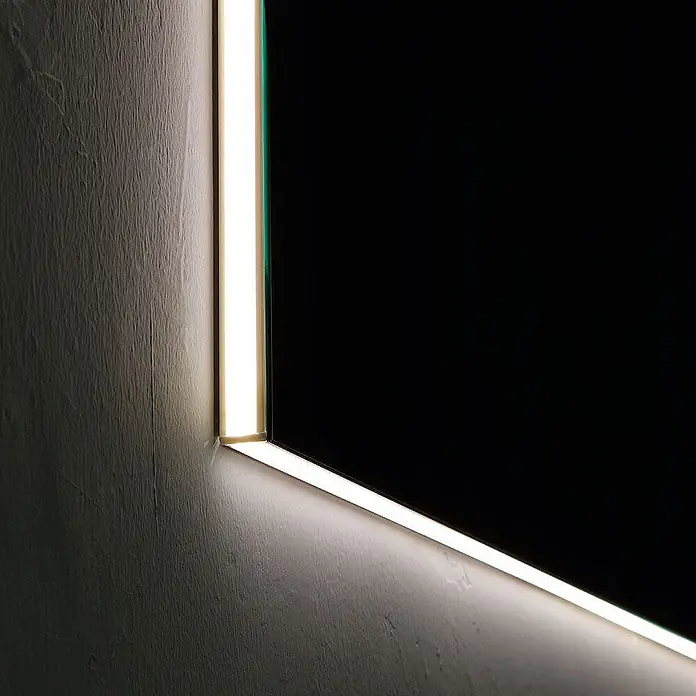 Kiamami Valentina Lichtspiegel - 25 x 700 cm, Farblos - Rechteckiger Spiegel mit integrierter LED-Beleuchtung entlang seiner vertikalen und horizontalen Kanten, beleuchtet eine strukturierte Wand.
