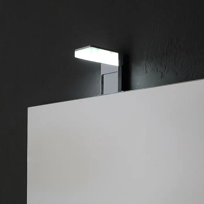 Kiamami Valentina Lichtspiegel - 20 x 700 cm, Farblos - Verchromte LED-Spiegelleuchte beleuchtet einen weißen Spiegel an einer dunklen Wand.