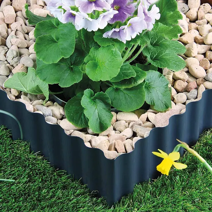Bellissa Rasenkante Welle - 500 x 20 cm, Anthrazit, Stahl - Dunkle, gewellte Gartenbegrenzung trennt ein Steinbeet von grünem Gras.
