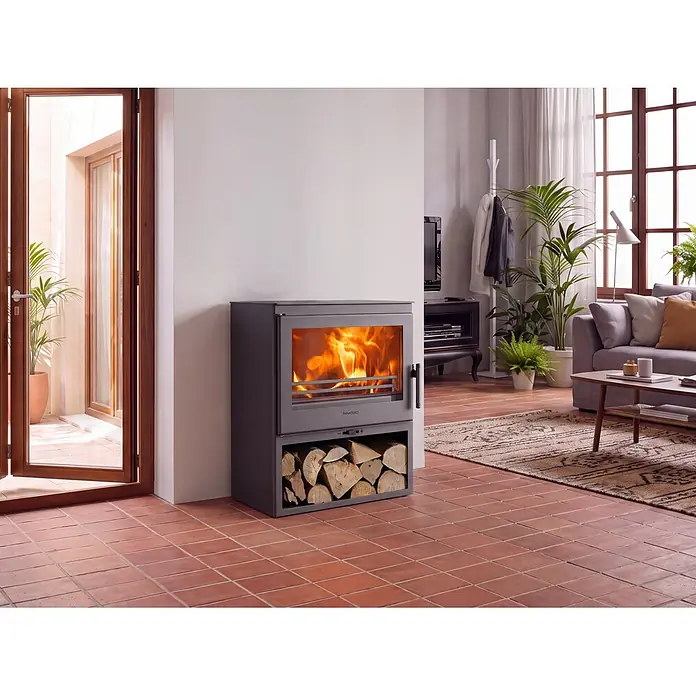 Panadero Estufa de leña Aitana - 7,4 kW, Volumen de calefacción: 220 m³, Negro - Estufa de leña gris oscuro con llamas visibles y almacenamiento de troncos, integrada en un acogedor salón con suelo de terracota.