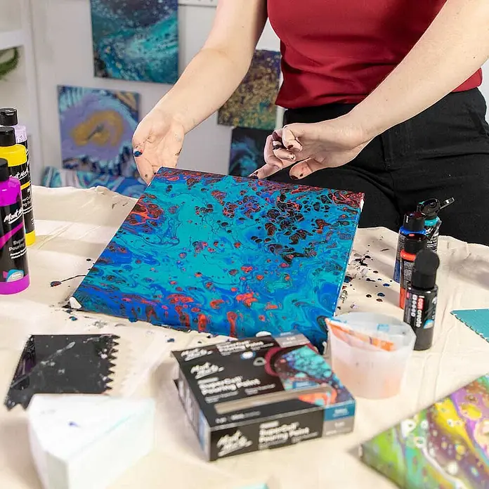 Mont Marte Acrylfarben-Set SuperCell® Galaxy - mehrfarbig, 4 Stk. x 60 ml, Flasche - Lebhaftes Acryl-Pouring-Gemälde auf Leinwand, umgeben von Pouring-Farben und Kunstzubehör, das kreative Anwendung zeigt.