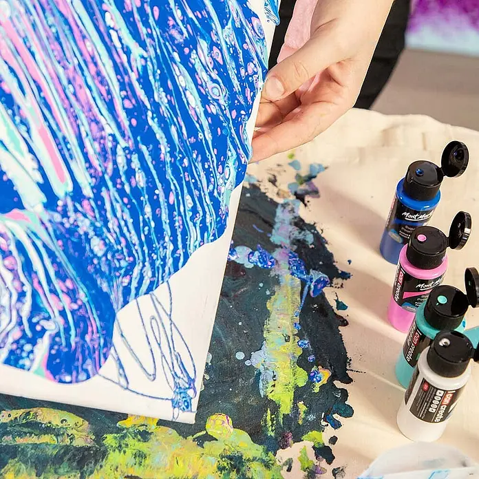 Mont Marte Acrylfarben-Set SuperCell® Tropical Ocean - mehrfarbig, 4 Stk. x 60 ml, Flasche - Hand hebt bemalte Leinwand mit blauer und pinker Pouring-Kunst, umgeben von Farbenflaschen auf bespritzter Fläche.