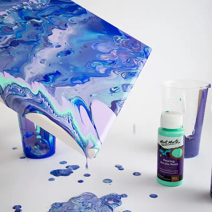 Mont Marte Acrylfarben-Set Premium Ethereal - mehrfarbig, 4 Stk. x 60 ml, Flasche - Flasche Mont Marte Pouring Acrylfarbe (Mintgrün) neben einer Leinwand, von der blaue, violette und mintgrüne Farbe tropft.