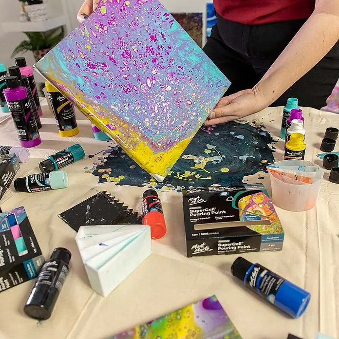 Mont Marte Acrylfarben-Set SuperCell® Coral Reef - mehrfarbig, 4 Stk. x 60 ml, Flasche - Person gießt lebendige Mont Marte SuperCell Pouring Paint von Leinwand, enthüllt faszinierendes abstraktes Muster mit 'Zellen'. Kunstzubehör umgibt.