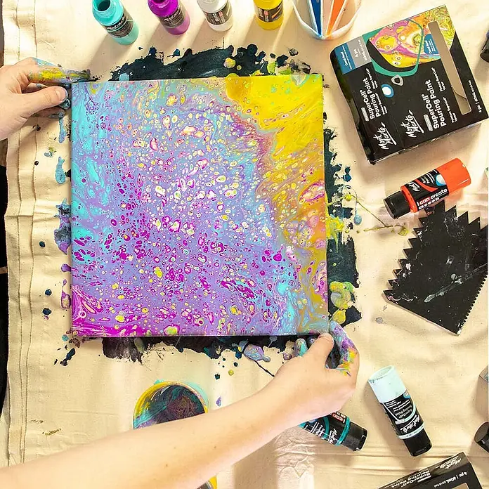Mont Marte Acrylfarben-Set SuperCell® Coral Reef - mehrfarbig, 4 Stk. x 60 ml, Flasche - Hände neigen eine Leinwand mit einem lebhaften, abstrakten Fluid-Art-Gemälde aus Gießfarbe.