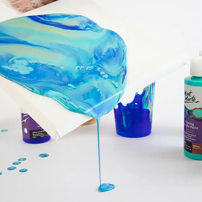 Mont Marte Acrylfarben-Set Premium Marina - mehrfarbig, 4 Stk. x 120 ml, Flasche - Blau-grüne Gießacrylfarbe wird auf eine weiße Leinwand gegossen, mit Mont Marte Farbflaschen in der Nähe.