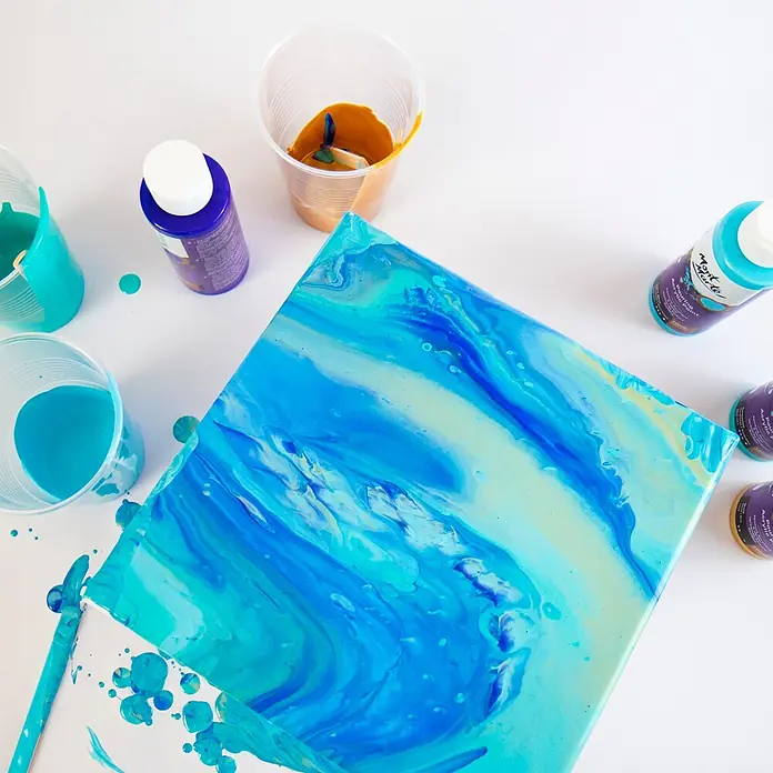 Mont Marte Acrylfarben-Set Premium Marina - mehrfarbig, 4 Stk. x 120 ml, Flasche - Acryl-Gießfarben in Blau-, Türkis- und Goldtönen, in Bechern gemischt und auf einer Leinwand für ein Fluid Art Kunstwerk verwendet.
