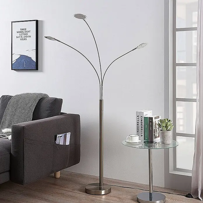Lindby Stehleuchte Anea - alu / grau / zink, alu / grau / zink - Eine Stehleuchte aus gebürstetem Metall mit drei geschwungenen Armen, jeder mit einem flachen, verstellbaren LED-Licht, in einem Wohnzimmer.