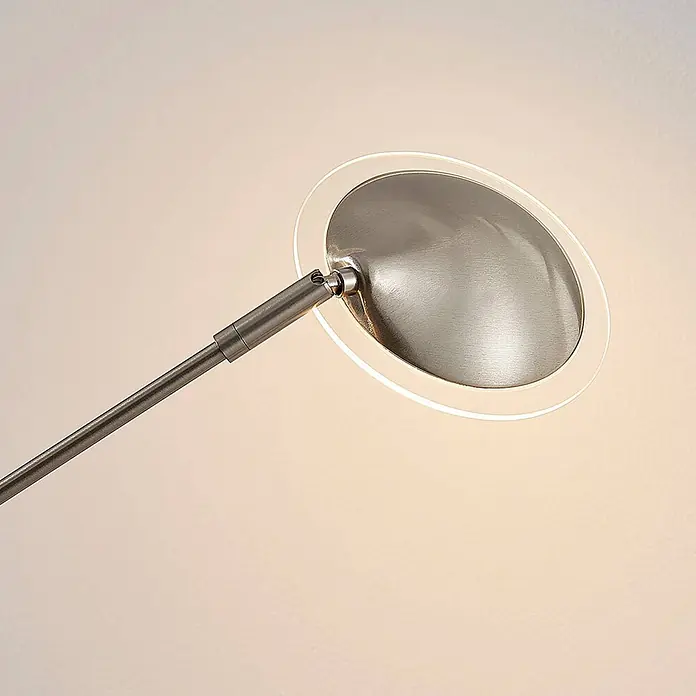 Lindby Stehleuchte Anea - alu / grau / zink, alu / grau / zink - Nahaufnahme eines modernen Leuchtenkopfes aus gebürstetem Metall mit leuchtendem Acrylring und reflektierender Scheibe, an einem Arm montiert.
