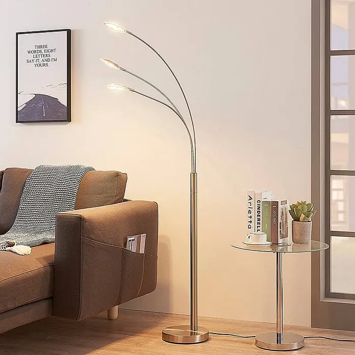 Lindby Stehleuchte Anea - alu / grau / zink, alu / grau / zink - Eine moderne Stehlampe mit gebürstetem Metall-Finish, drei geschwungenen Armen und beleuchteten LED-Leuchten im Wohnzimmer platziert.