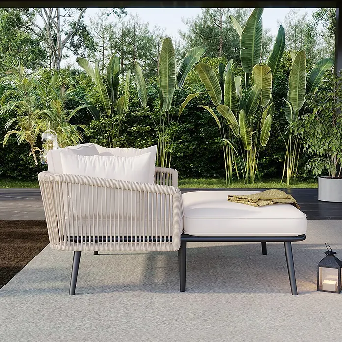 SONNENH Garten-Loungesessel - 1 Stk., Polyester, Beige - Beiger Outdoor-Sessel und passender Hocker mit weißen Kissen auf einer Terrasse, umgeben von üppig grünen Pflanzen.