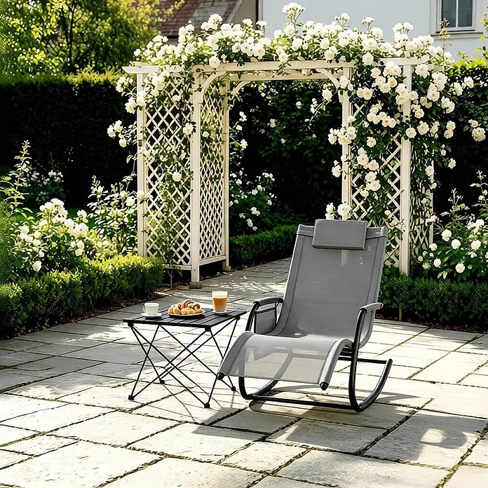 SONNENH Garten-Schaukelstuhl - 1 Stk., Metall, Polyester, Grau, B x T x H: 152 x 62 x 83 cm - Grauer Stoff-Schaukelliegestuhl und kleiner schwarzer Beistelltisch auf einer Steinterrasse in einem sonnigen Rosengarten.