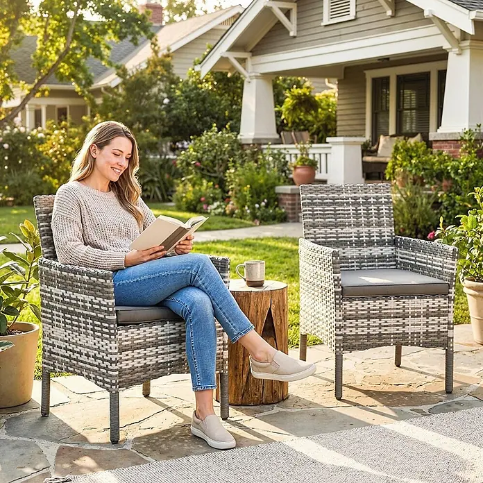 SONNENH Gartenstuhl-Set - 2 Stk., Rattan, Grau, B x T x H: 62 x 58 x 87 cm - Zwei grau-weiße Outdoor-Geflechtsessel mit dunkelgrauen Kissen. Eine Frau entspannt und liest in einem Sessel auf der Terrasse.