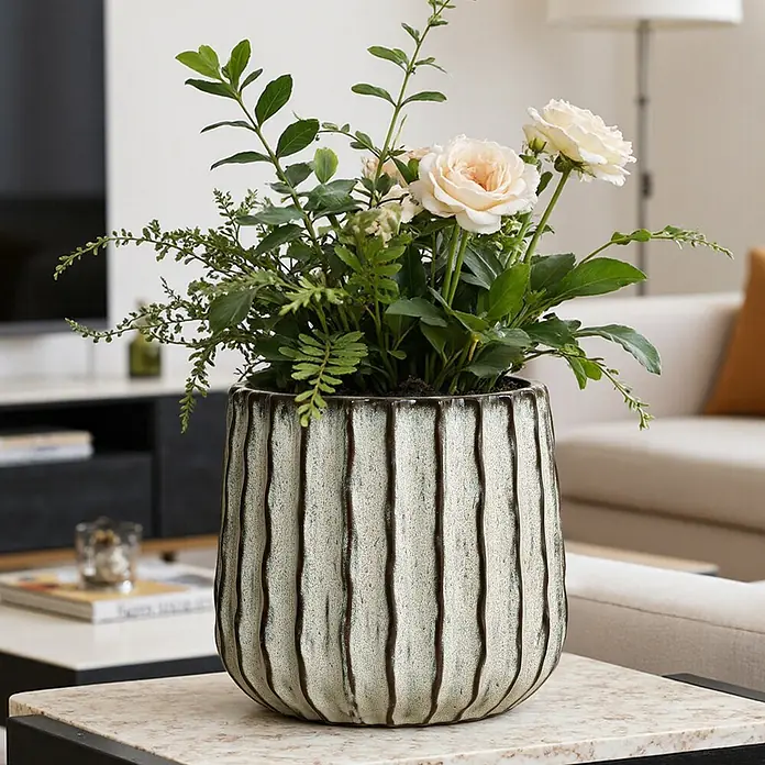 Hometopia Pflanztopf HTPL0078-LW - 1 Stk., Außenmaß (Ø x H): 23,5 x 2,61 cm, Keramik, Salbeigrün - Gerippter Keramik-Pflanztopf, cremefarben mit dunklen vertikalen Linien, gefüllt mit Grünpflanzen und hellrosa Rosen, auf einem hellen Marmortisch.