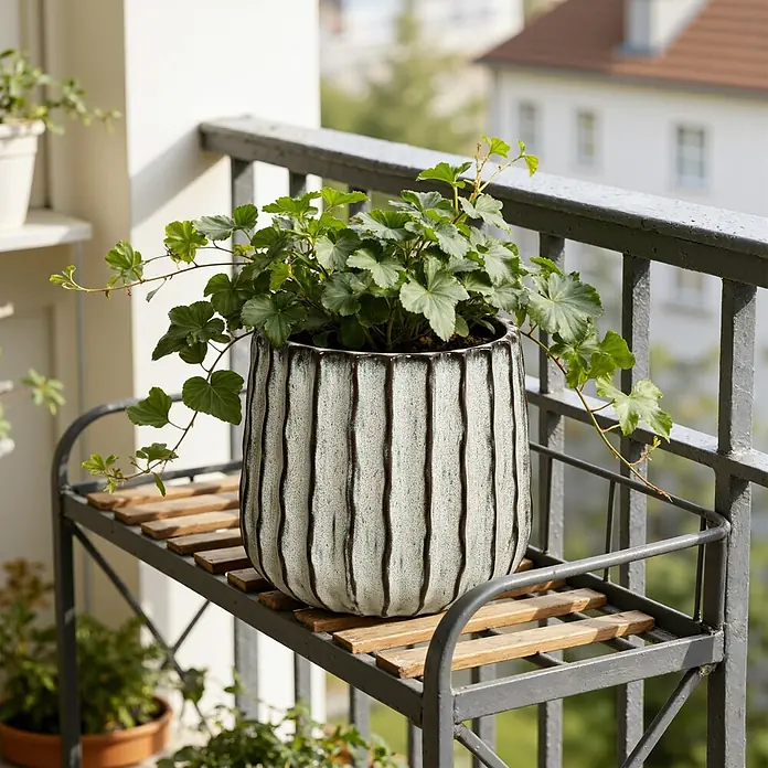 Hometopia Pflanztopf HTPL0078-LW - 1 Stk., Außenmaß (Ø x H): 23,5 x 2,61 cm, Keramik, Salbeigrün - Strukturierter weißer Pflanztopf mit dunklen vertikalen Streifen, der eine grüne Pflanze enthält, auf einem Metall-Pflanzenständer auf einem Balkon.