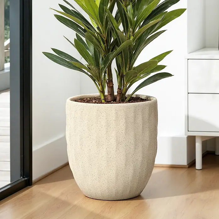 Hometopia Pflanztopf HTPL0183 - Außenmaß (Ø x H): 34 x 34 cm, Verbundwerkstoff, Apricot - Ein strukturierter hellbeiger Pflanztopf mit vertikalen Rillen und einer grünen Pflanze steht auf einem Holzboden neben einem Fenster.
