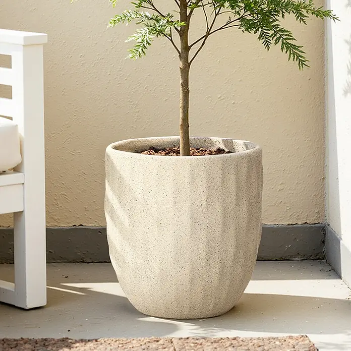 Hometopia Pflanztopf HTPL0183 - Außenmaß (Ø x H): 34 x 34 cm, Verbundwerkstoff, Apricot - Heller, gesprenkelter, texturierter Pflanzkübel mit grüner Pflanze, auf einer Terrasse neben einem weißen Stuhl.
