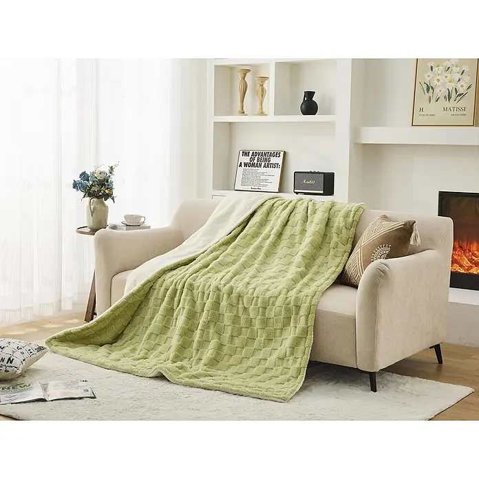 Purline Manta eléctrica Warmer Bed Plus 2 - 160 W, 180 x 160 cm - Una manta verde claro texturizada con patrón a cuadros, drapada sobre un sofá beige en una sala acogedora.