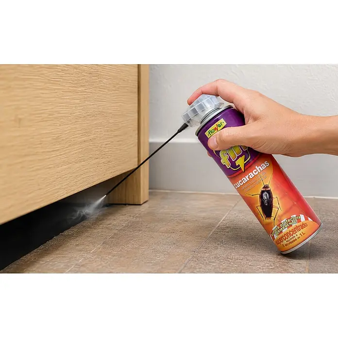 Flower Spray anti-insectos rastreros Fin - 800 ml - Mano rociando insecticida morado y rojo para cucarachas en una rendija del armario.