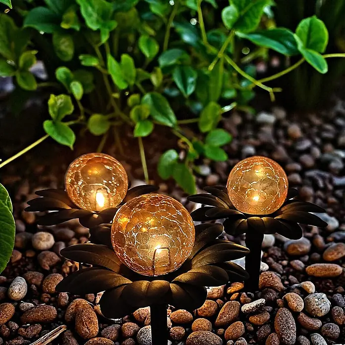 DAPO Solar-Dekoleuchte Flora mit Kugel in Bernsteinoptik - L x B x H: 15 x 15 x 20 cm, Rostfarbig - Drei Solar-Gartenleuchten mit rissigen Glaskugeln, warm leuchtend in blumenförmigen Sockeln zwischen Gartenkieseln.