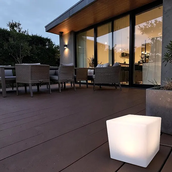 DAPO Solar-Dekoleuchte LED Solar-Leuchte Mate Würfel 30cm - L x B x H: 30 x 30 x 30 cm, Weiß, IP67 - Eine leuchtende weiße Würfelleuchte steht auf einer Holzterrasse und beleuchtet den Außenbereich in der Dämmerung.