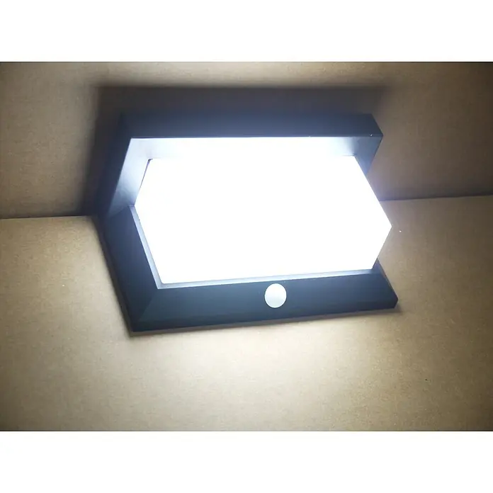 DAPO Solar-Außenwandleuchte Solar-Wandleuchte "All weather" - L x B x H: 9 x 21 x 12 cm, IP44 - Schwarze, rechteckige LED-Leuchte mit heller weißer Fläche und Bewegungssensor, montiert auf einer braunen Oberfläche.
