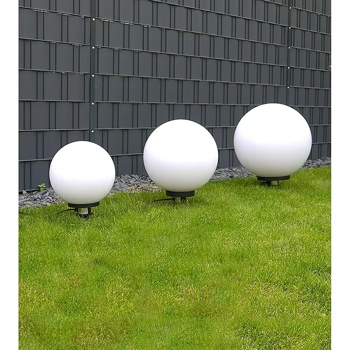 Kugelleuchte Marlon 40 cm -  - Drei weiße kugelförmige Gartenleuchten unterschiedlicher Größe auf Rasen vor einem dunklen Zaun.