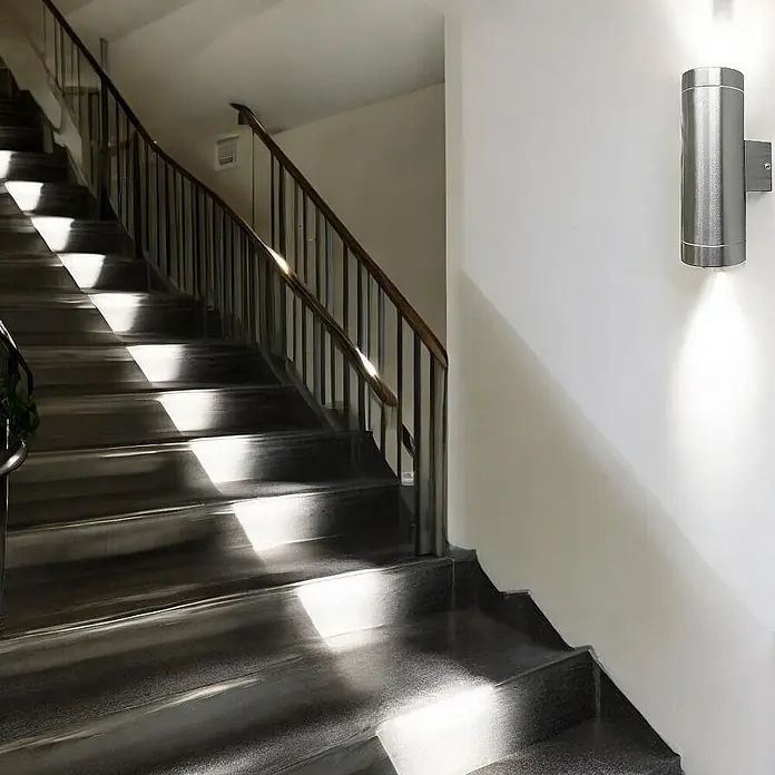 DAPO Außenwandleuchte Außen-Wandleuchte Bergen Edelstahl - 70 W, 10,5 x 7,6 x 21 cm, Silber, IP44 - Zylindrische Wandleuchte aus gebürstetem Edelstahl beleuchtet eine Treppenhauswand nach oben und unten.
