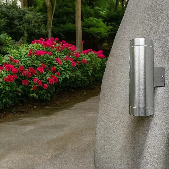 DAPO Außenwandleuchte Außen-Wandleuchte Bergen Edelstahl - 70 W, 10,5 x 7,6 x 21 cm, Silber, IP44 - Gebürstete Edelstahl-Auf- und Ab-Wandleuchte an Außenwand, Blick auf Gartenweg mit roten Blumen.