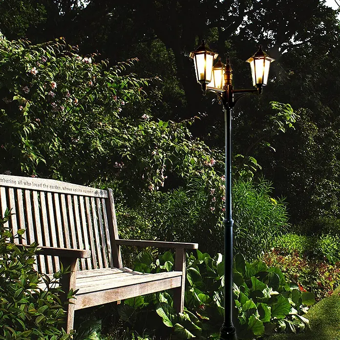 DAPO Kandelaber Kingston 3 flg. schwarz - Farbe Gehäuse: Schwarz, 26 x 26 x 200 cm, Ohne Leuchtmittel - Schwarze dreiflammige Gartenlaterne mit leuchtenden Lichtern, beleuchtet eine Gartenszene mit Holzbank.