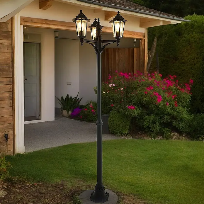 DAPO Kandelaber Kingston 3 flg. schwarz - Farbe Gehäuse: Schwarz, 26 x 26 x 200 cm, Ohne Leuchtmittel - Schwarze dreiflammige Außenlaterne aus Metall beleuchtet einen Gartenweg neben einem Haus.