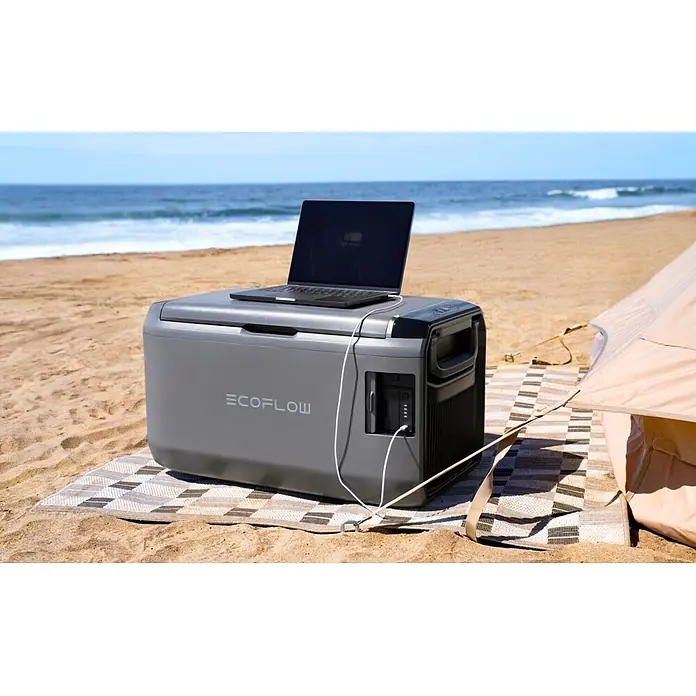EcoFlow Akku-Kühlbox Glacier - 1 Akku, L x B x H: 48 x 70,6 x 40 cm, 45 l - Graue EcoFlow Powerstation/Kühlbox auf einem Strand, lädt einen Laptop. Ein Zelt ist daneben.