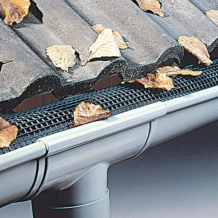 Marley Laubstop - Nennweite: 100 mm - 125 mm, Länge: 200 cm - Nahaufnahme einer Dachrinne mit einem schwarzen Gittersieb und Herbstlaub. Das Sieb schützt die Rinne vor Verstopfung.