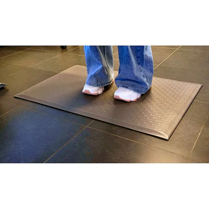 Proregal Gummimatte Anti-Ermüdungsmatte COMFORT PLUS 91x300cm Grau - 300 x 91 cm, Grau - Person steht auf einer dunklen, texturierten Anti-Ermüdungsmatte, die ihre ergonomische Nutzung zeigt.