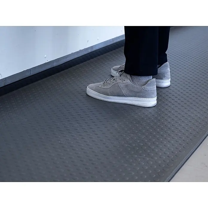 Proregal Gummimatte Anti-Ermüdungsmatte COMFORT PLUS 91x300cm Grau - 300 x 91 cm, Grau - Dunkelgraue Matte mit erhabenen Ovalmustern, auf der eine Person in grauen Turnschuhen steht.