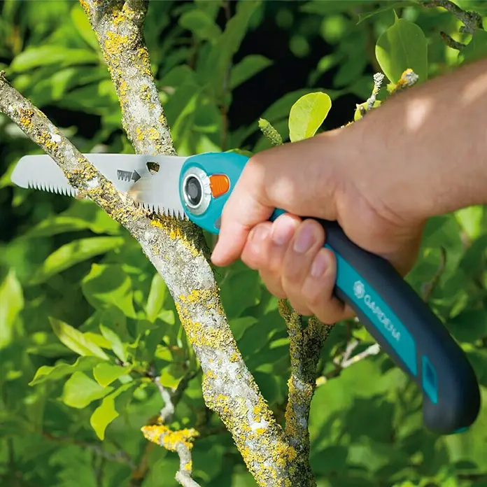 Gardena Garten-Klappsäge 200 P - Länge: 291 mm - Nahaufnahme einer Gardena Astsäge in Aktion, die einen Baumzweig durchtrennt, umgeben von grünem Laub.