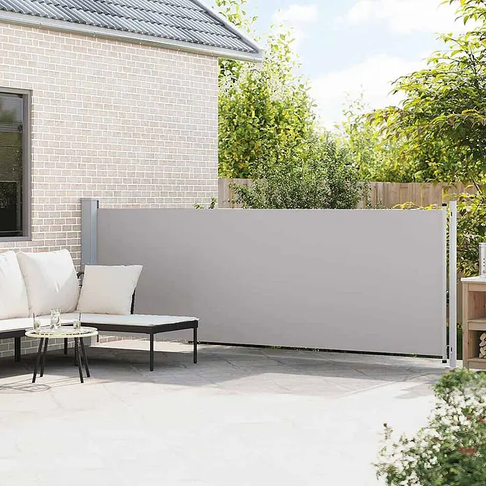 VidaXL Klemmmarkise - Grau, Breite: 6 m, Ausfall: 6 m - Helles graues ausziehbares Seitenmarkise auf einer Terrasse, das Privatsphäre neben einem Haus bietet.