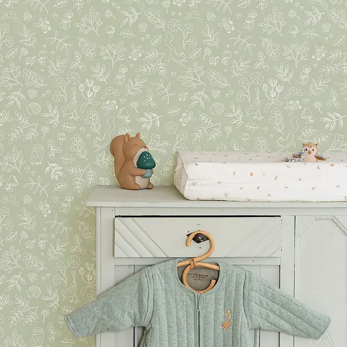 Little Dutch Vliestapete Waldwunder - Grün/Weiß, Floral, 10 x 0,53 m - Hellgrüner gesteppter Babyschlafsack mit Eichhörnchen-Stickerei, an Holzbügel auf weißem Schrank hängend.