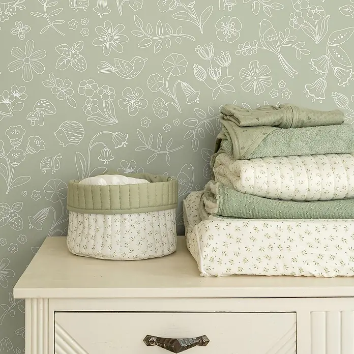 Little Dutch Vliestapete Waldwunder - Grün/Weiß, Floral, 10 x 0,53 m - Gestapelte grüne und weiße Babytextilien und passender Korb auf einer Kommode im Kinderzimmer.