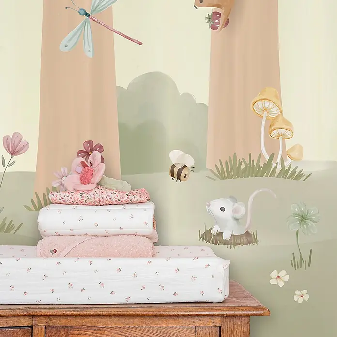 Little Dutch Fototapete Zaubergarten - Vlies - Stapel weißer und rosa Babytextilien mit Blumenmuster, inklusive Wickelauflagenbezug und Decken, auf einem Holztisch im Kinderzimmer.