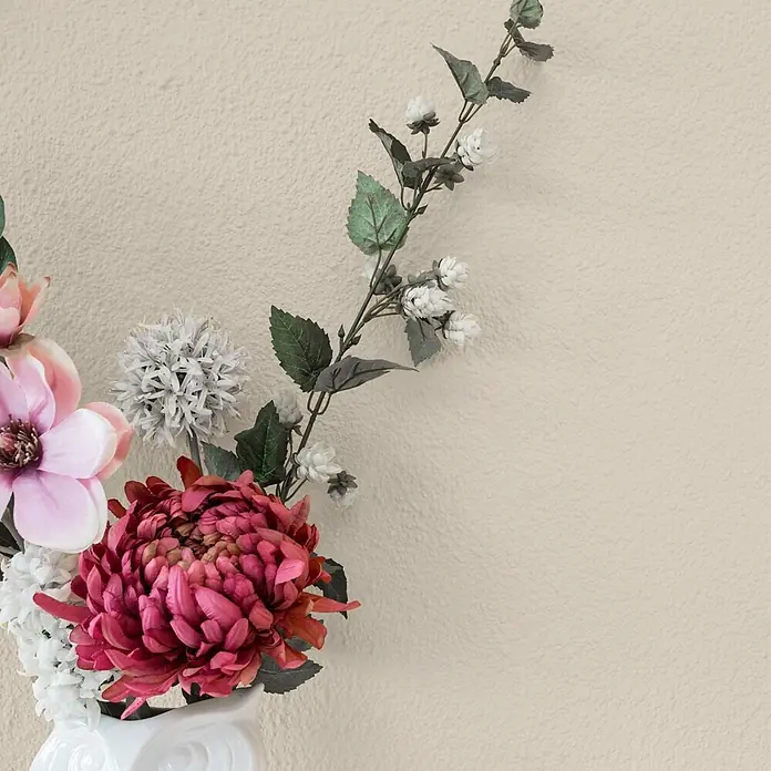 Bricoflor Wandfarbe 2,5 Liter, Sand - creme beige, Matt, 2,5 l, Wasserverdünnbar - Künstlicher Blumenstrauß mit rosa, fuchsiafarbenen und weißen Blüten in einer weißen Vase vor einer strukturierten Wand.