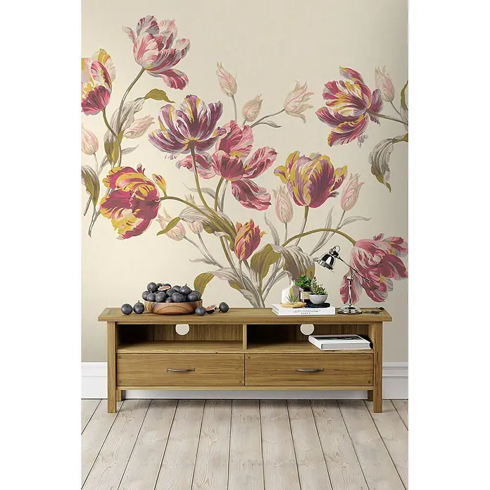 Laura Ashley Fototapete Gosford - Vlies - Eine hellbraune TV-Konsole aus Holz mit zwei Schubladen und offenen Fächern, dekoriert mit Gegenständen, vor einer floralen Tapete.