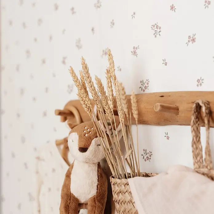 Little Dutch Vliestapete Feenblume - Rosa/Weiß, Tieroptik, 10 x 0,52 m - Getrocknete goldene Weizenähren in einem Korb neben einem braunen Hirsch-Stofftier auf rustikaler Holzleiste vor floraler Wand.